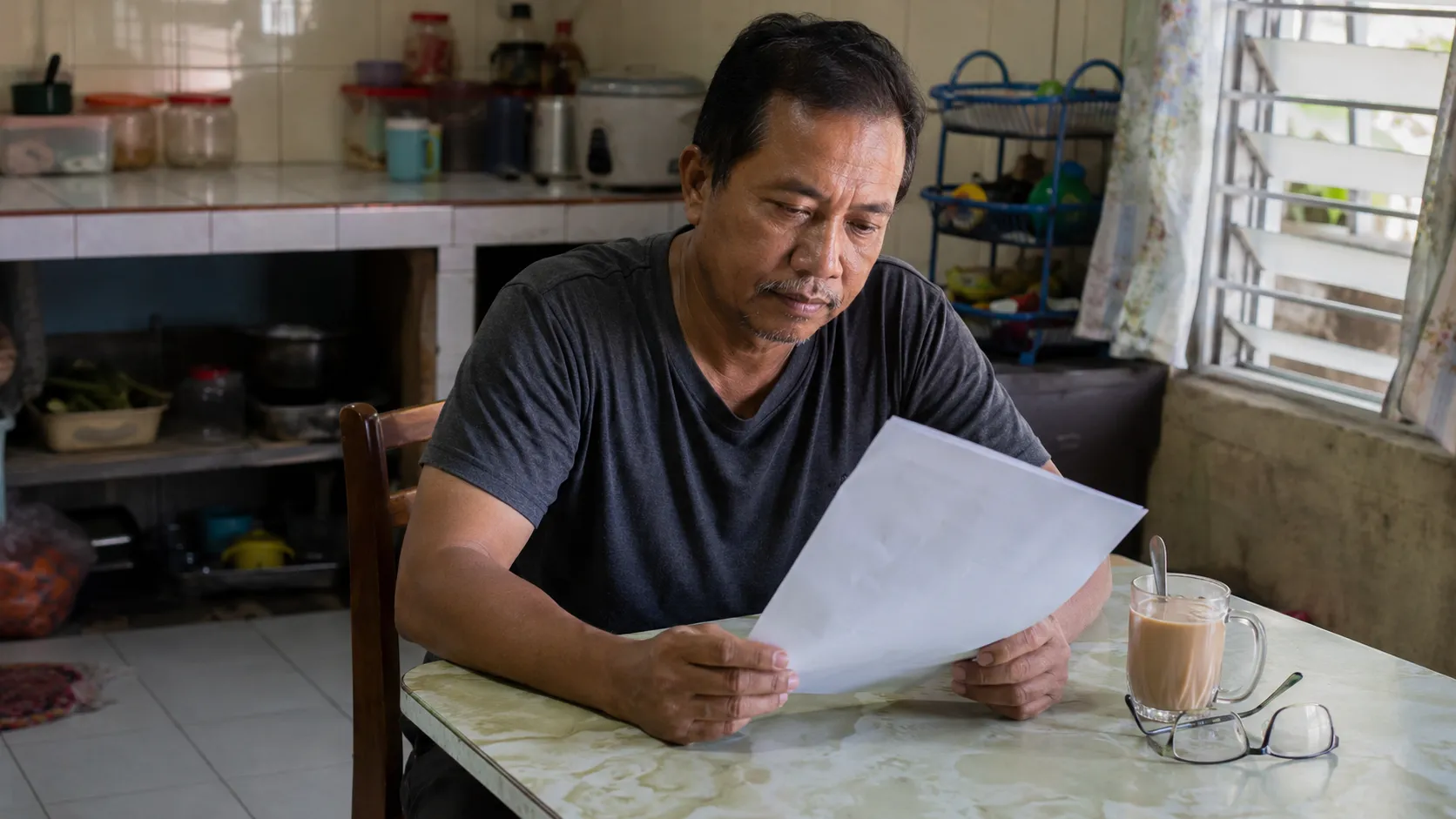 A Malaysian household reviewing an EPF and unit-trust savings statement at the kitchen table in morning light