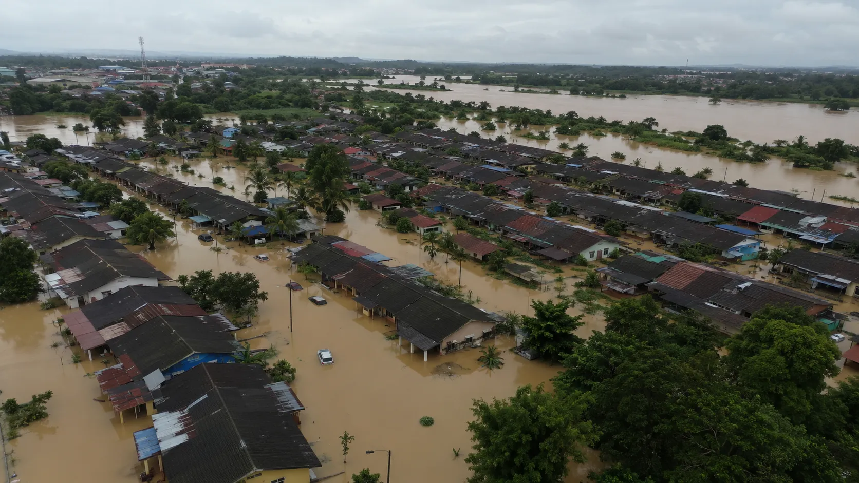 Aerial view of a Malaysian residential neighbourhood beside a river, the water swollen brown and encroaching on the houses