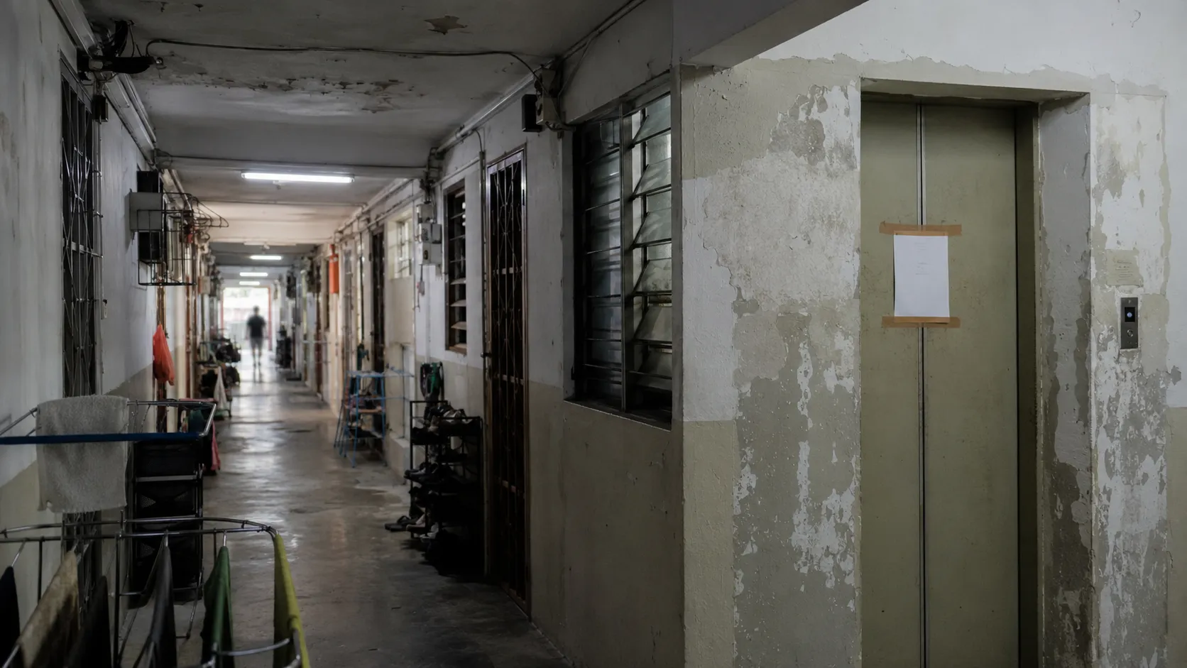 A worn, dimly lit condo corridor with peeling paint and cluttered doorways, the kind found in an investor-heavy student block