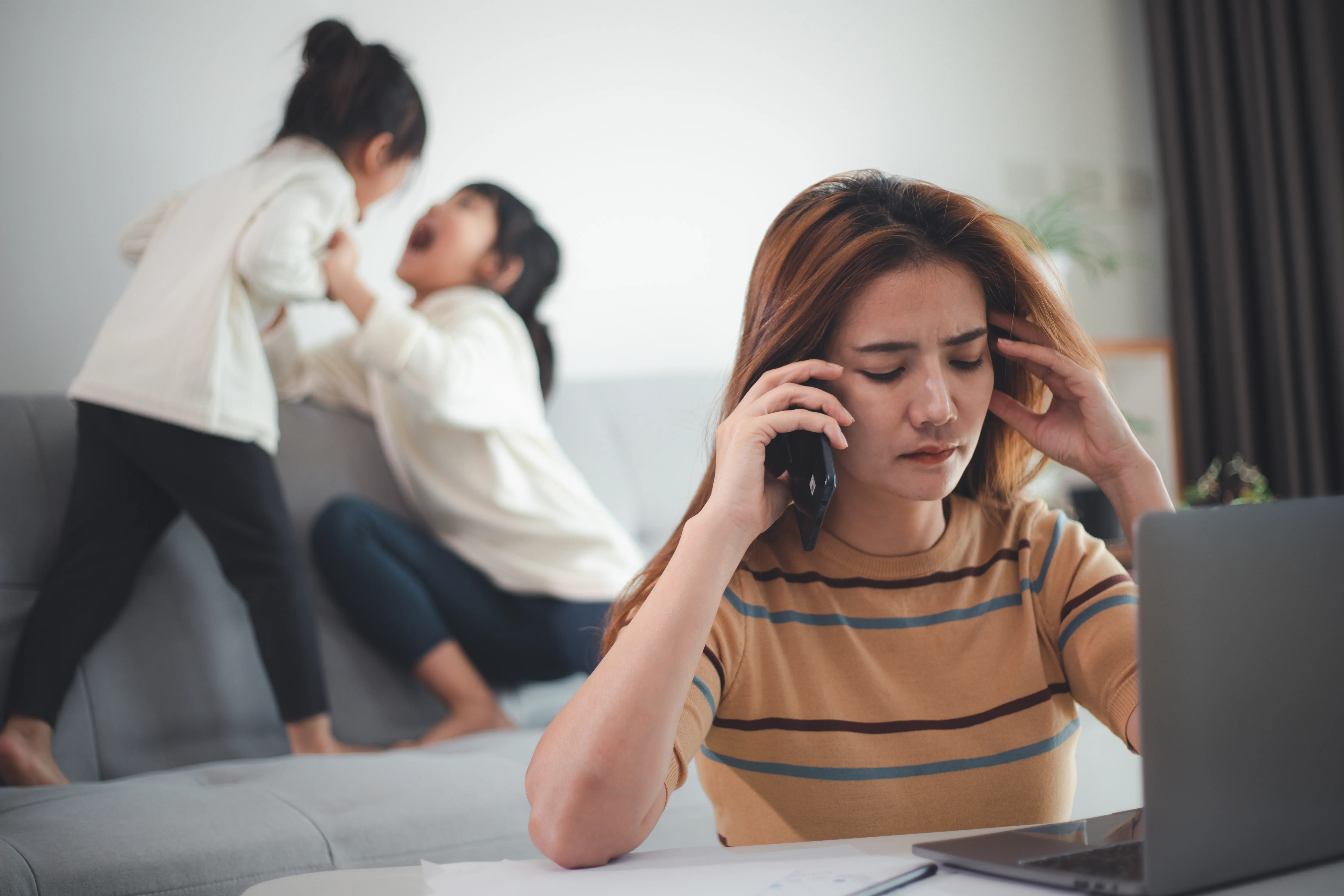 A woman on her phone while her two daughters play fight in the background