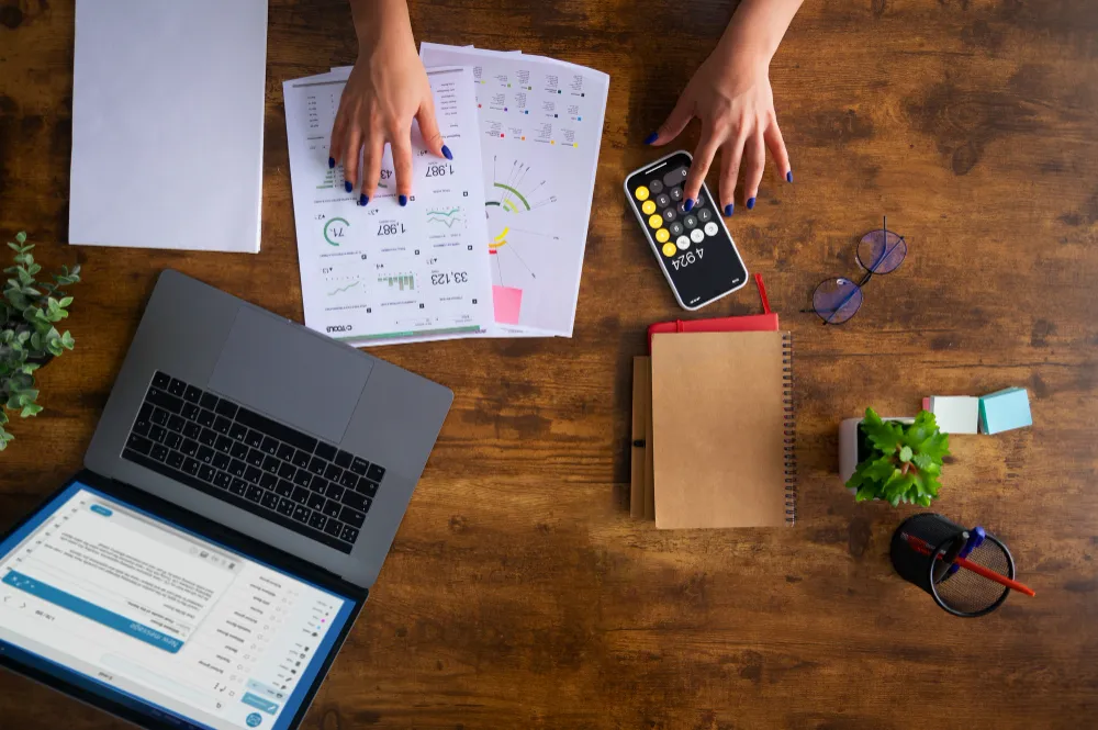 Hands over a finance expense sheet while holding a calculator on a wooden desk