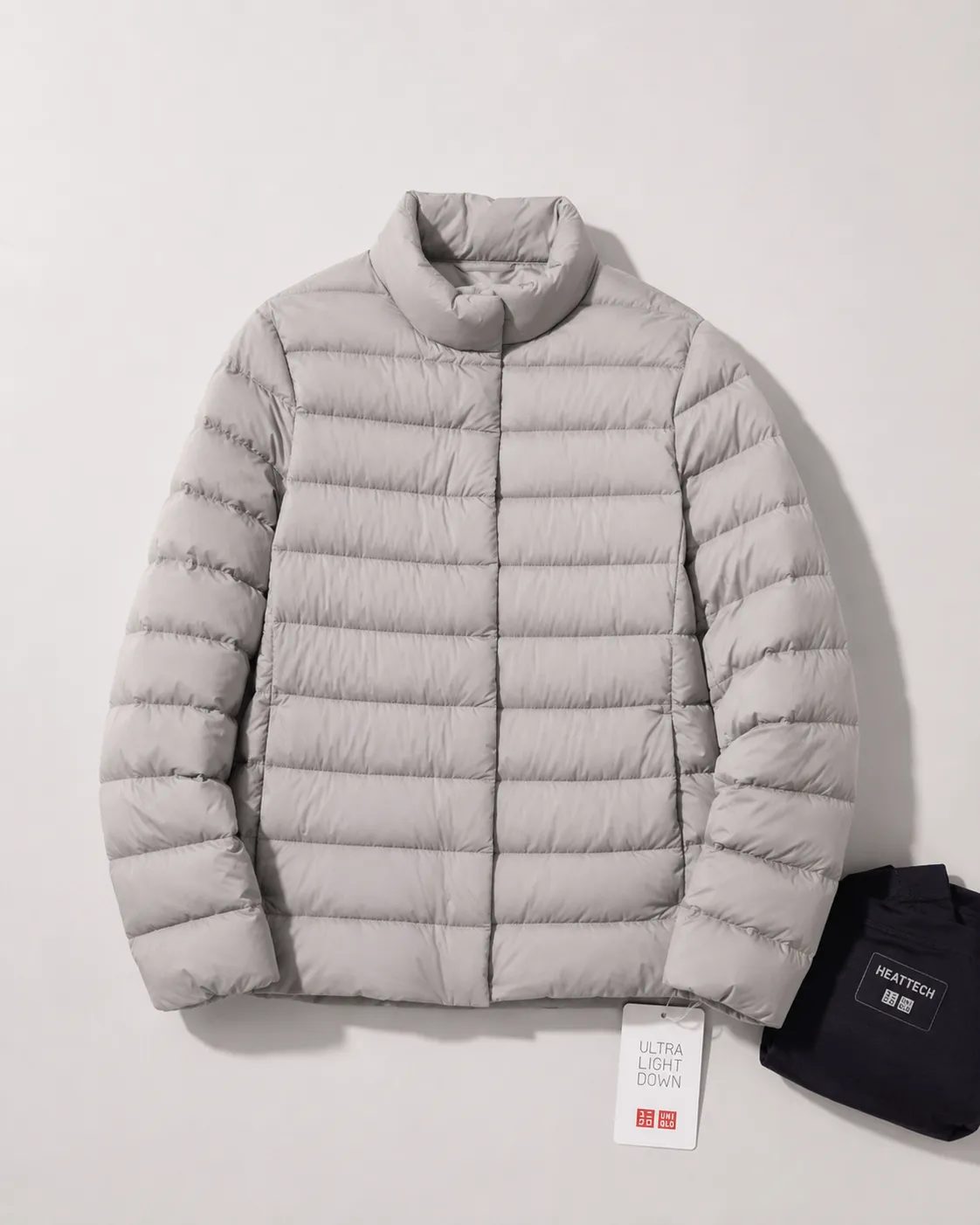 A Uniqlo Ultra Light Down jacket being compressed into its palm-sized pouch beside a HeatTech top